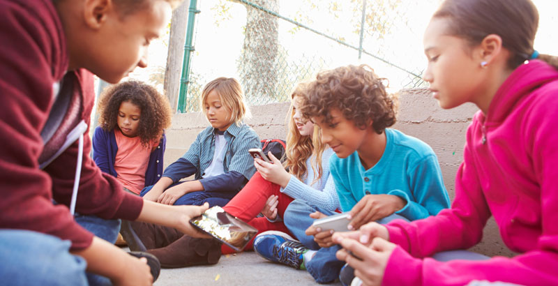 Jugendliche sitzen im Freien und spielen mit ihren Handys.