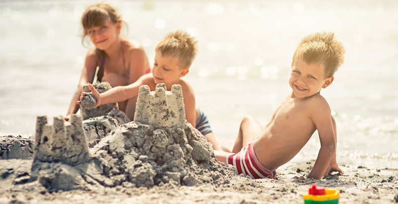 Kinder sitzen am Strand und bauen eine Sandburg.
