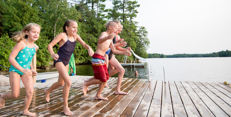 Kinder springen von einem Steg in einen Natursee.