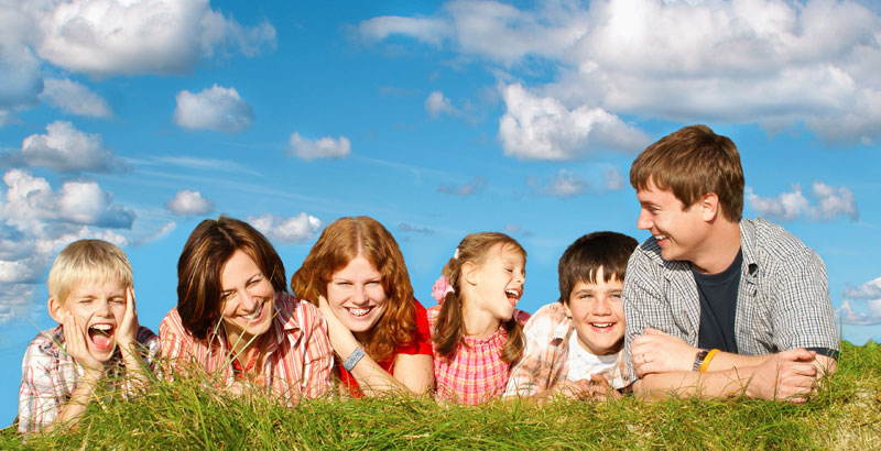 Eine Familie mit vier Kindern liegt lachend im Gras.