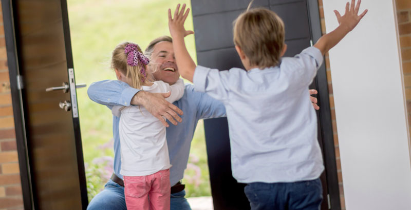 Zwei Kinder begrüßen ihren Papa freudig an der Tür.