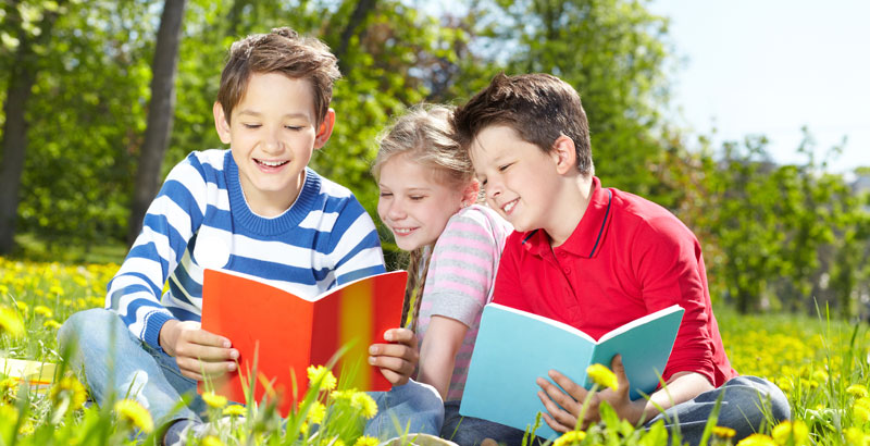 Kinder sitzen lesend auf einer Wiese.