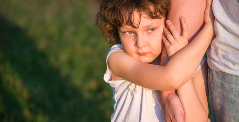 Ein Mädchen hält sich ängstlich am Unterarm seiner Mutter fest.